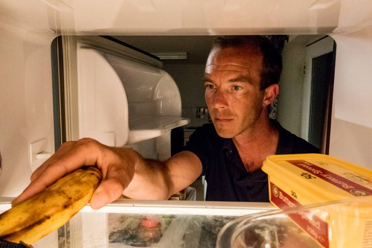 A man reaches into the fridge for a banana.