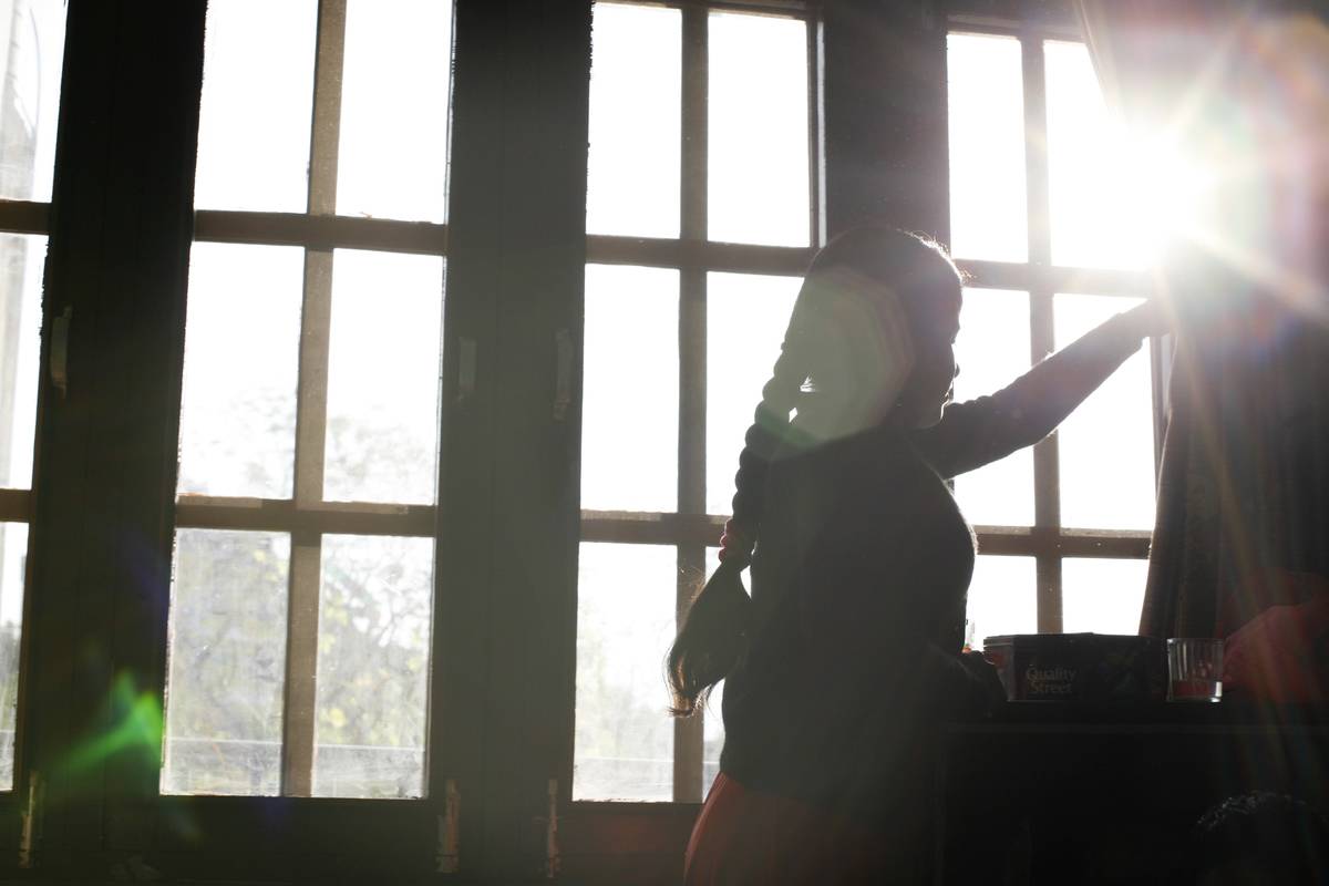 A woman opens window curtains to let the light in.