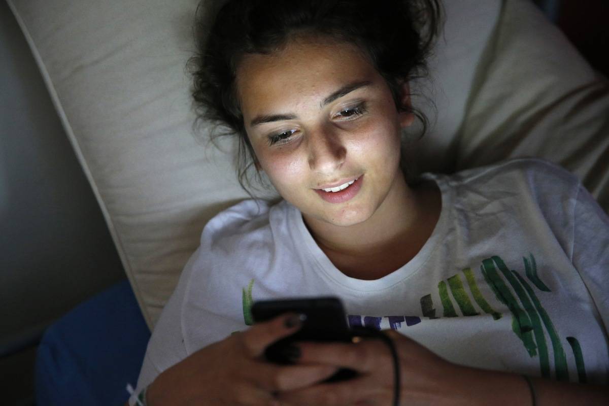 A woman scrolls through her phone in bed.