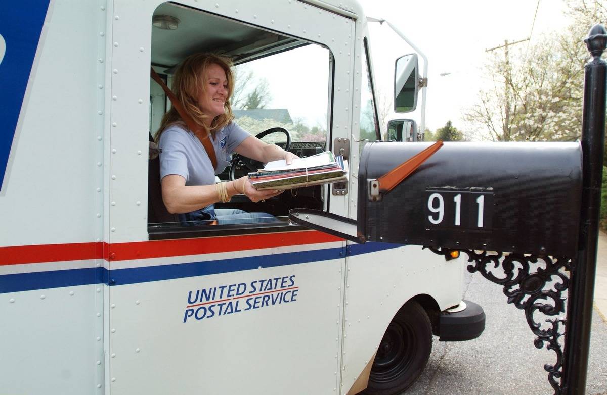A postal worker puts mail into a mailbox.