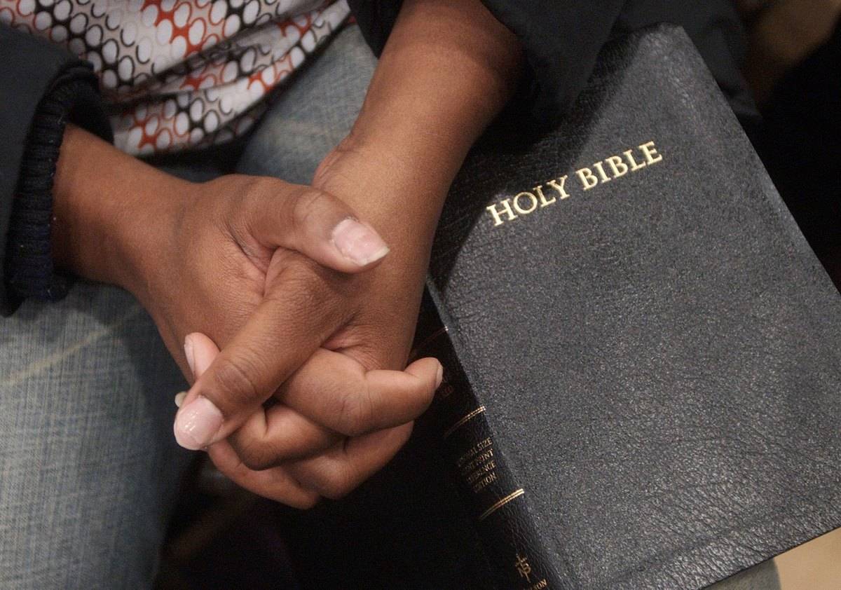 A woman clasps her hands in prayer on top of a Bible.