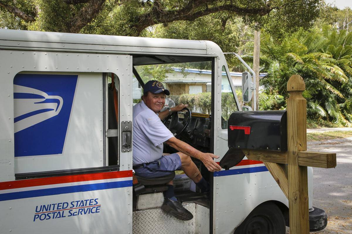 A postal worker smiles while checking a person's mailbox.