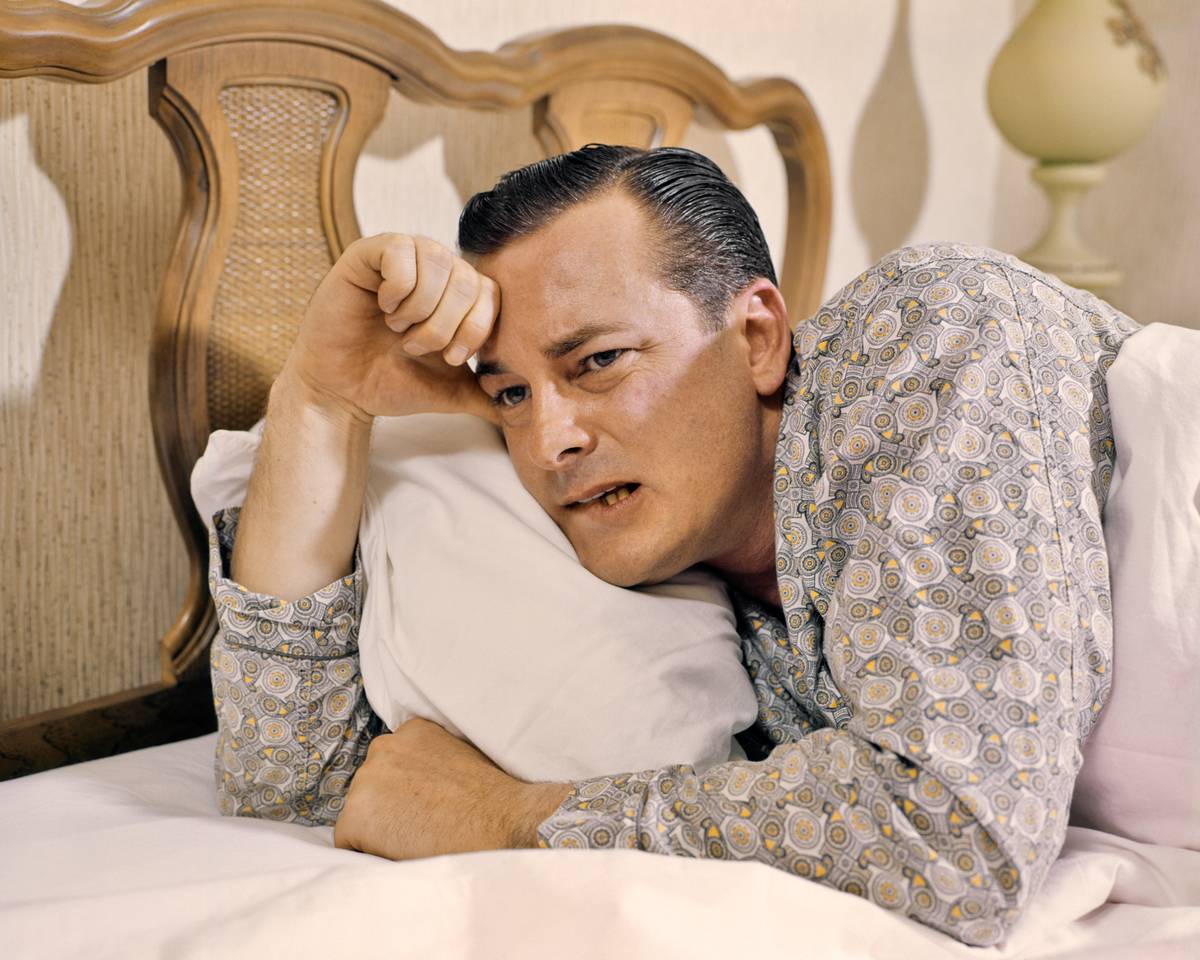 A man sits up in bed, tired and groggy.