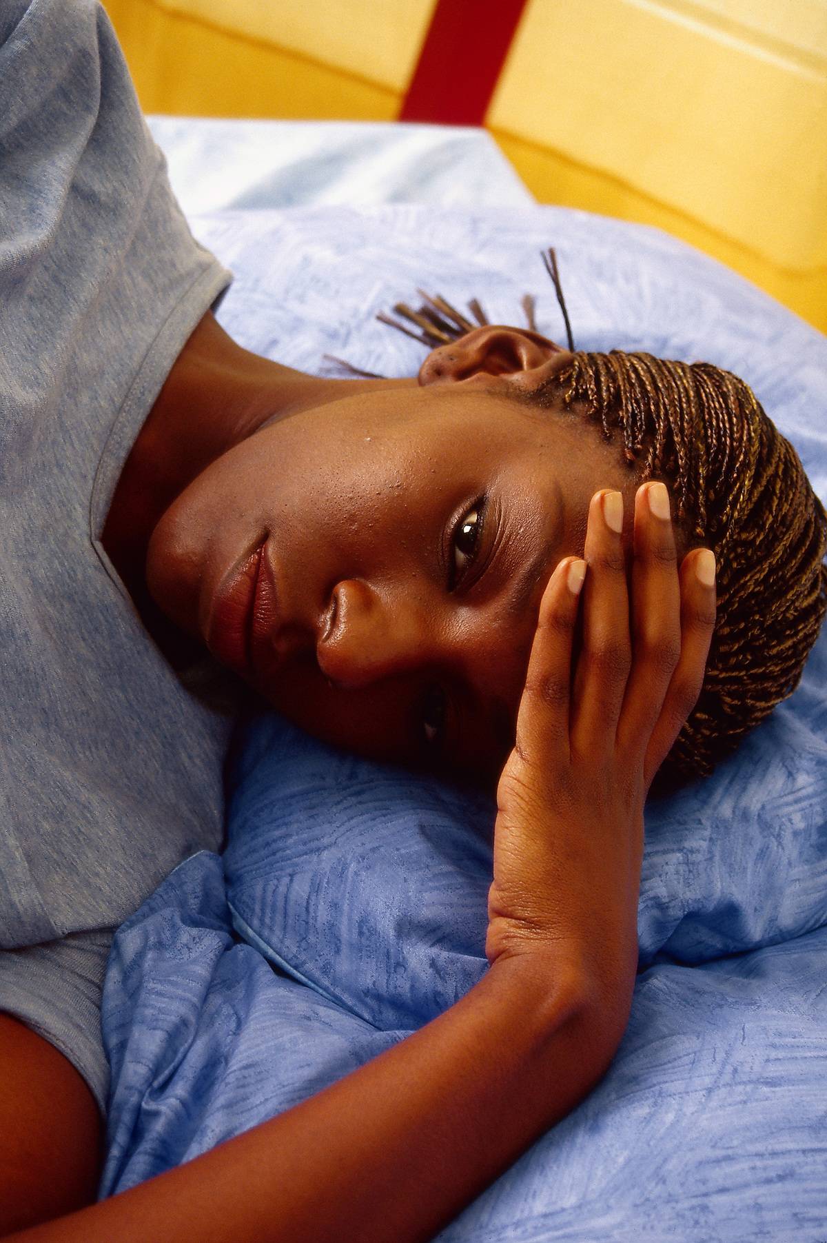 A woman tiredly presses her hands against her forehead in bed.