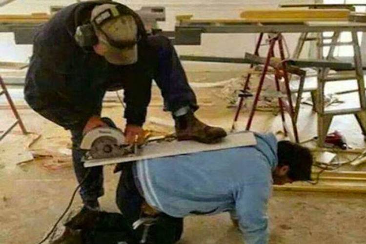 Person using a saw while having the board up against another man's back