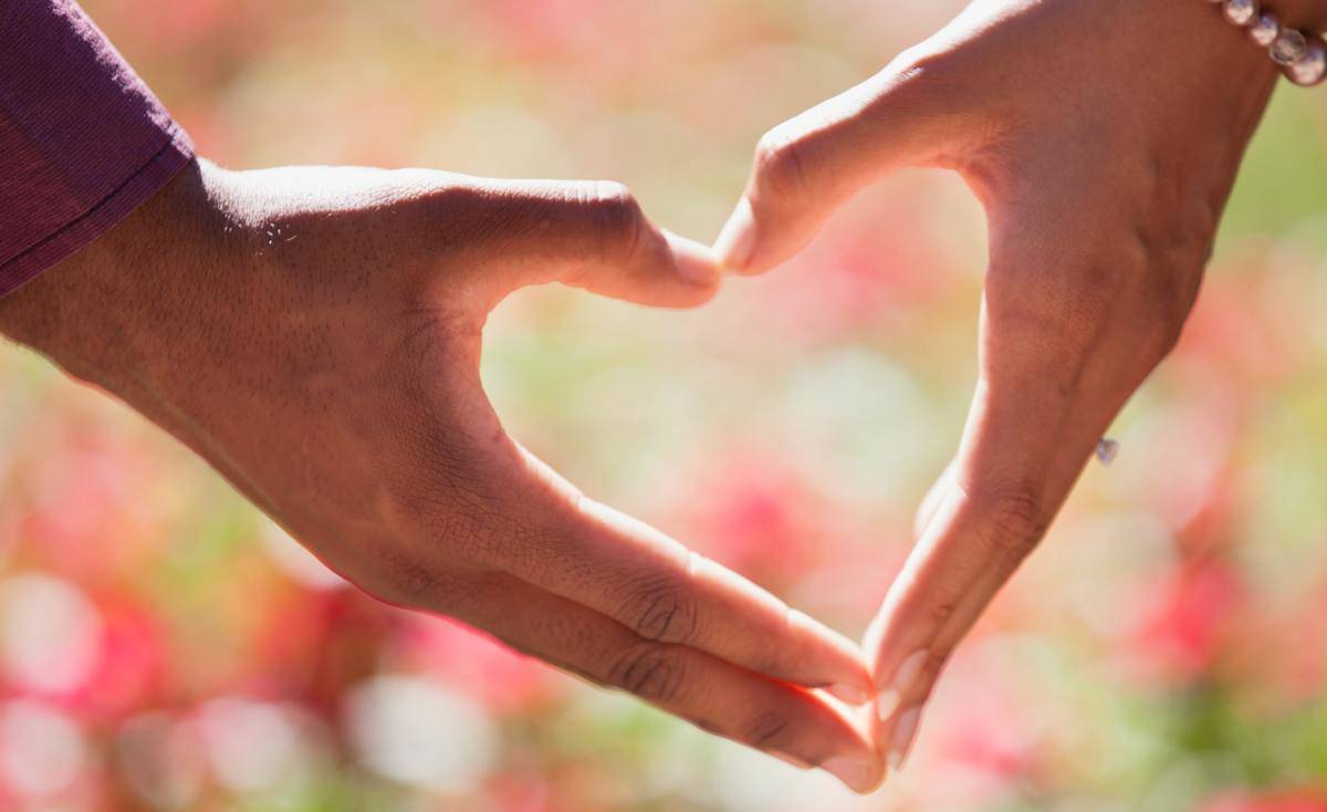 A couple makes a heart using their hands. 