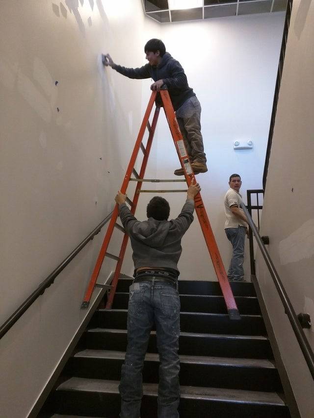 Man on ladder on the stairs and the ladder is being held up by another person