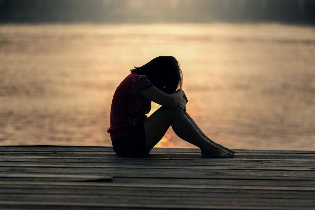 Woman sits by herself on a dock overlooking a lake at sunset.