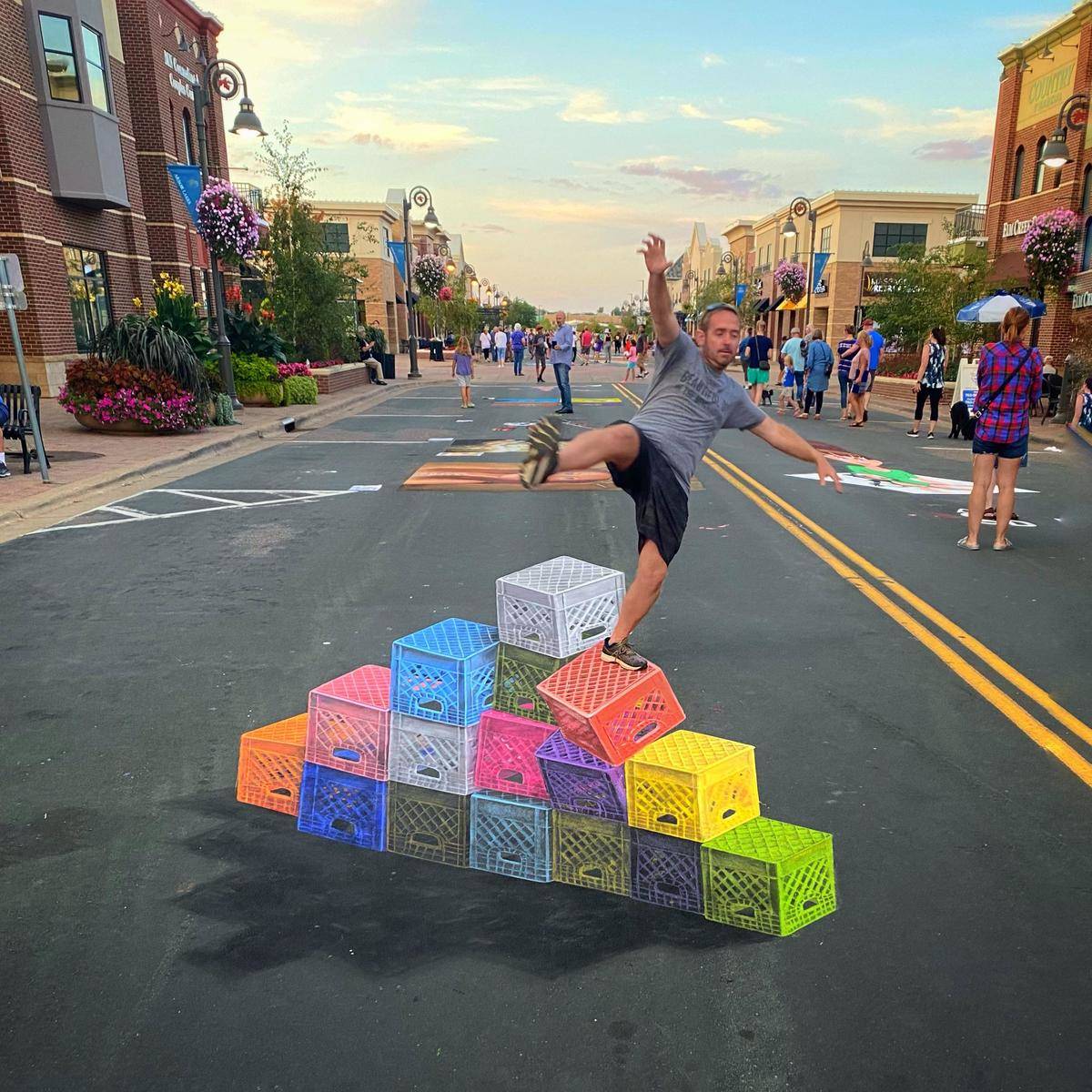 Milk crates drawn out of multi-colored chalk, man posing standing on chalk mural, looks like he's falling