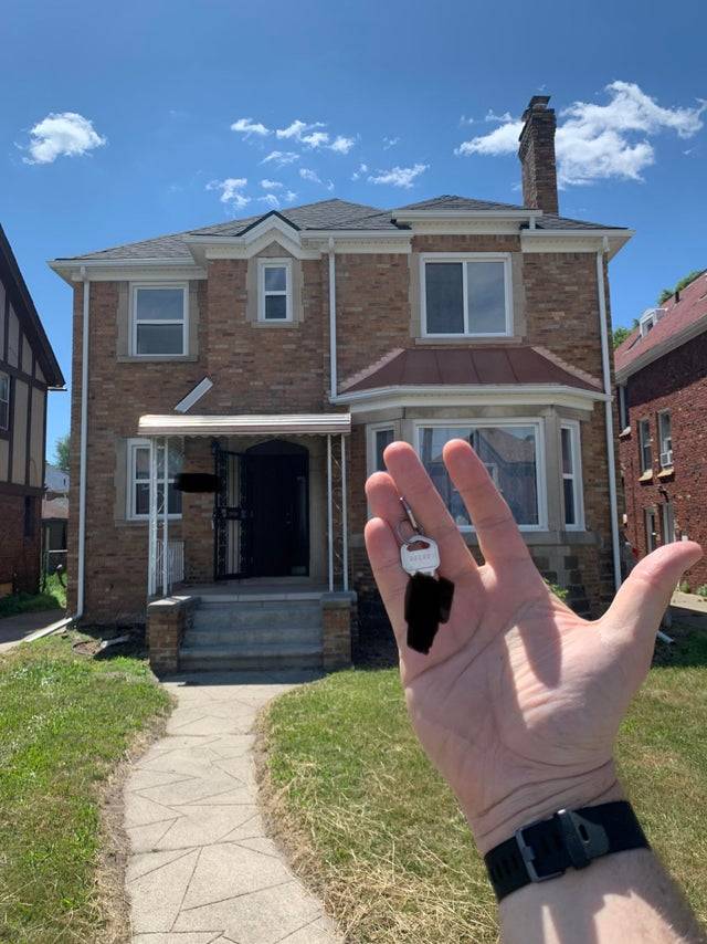 Photo of a man holding up a set of keys in front of the new home he and his wife just purchased.