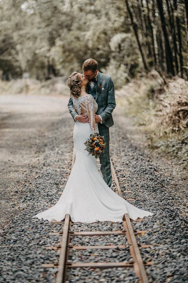 Photo of a newlywed couple kissing in a forest on their wedding day