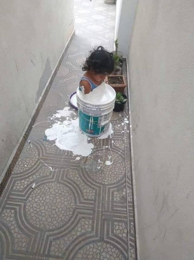 Child sitting in a pail of paint with it spilling onto the floor.