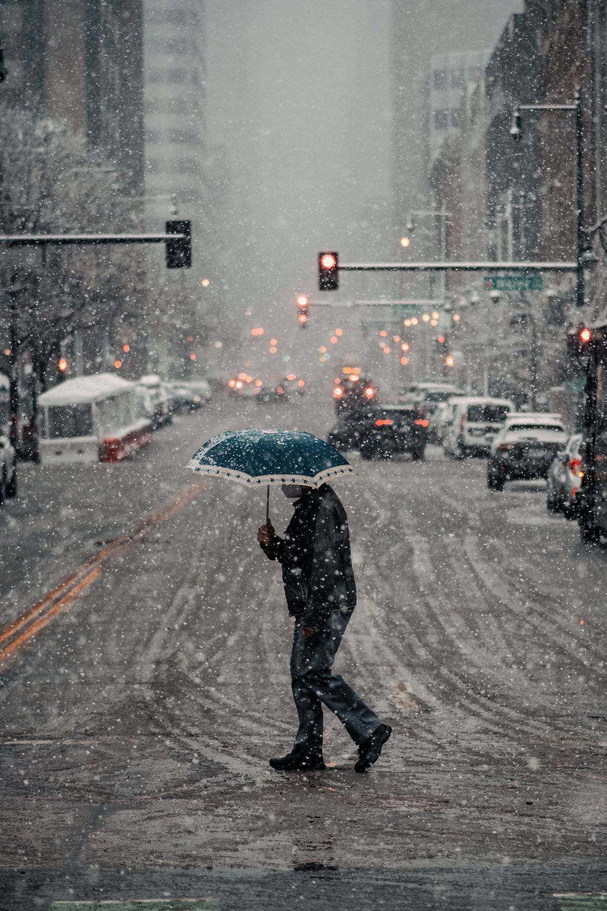 Man walks through the street during a snowfall while holding a teal umbrella
