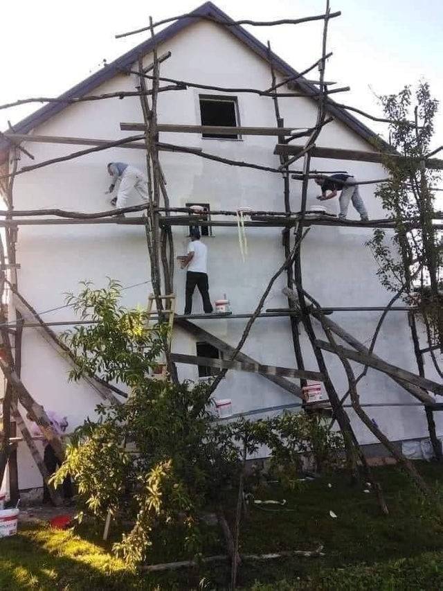 Scaffolding on side of house made out of tree branches with workers on it