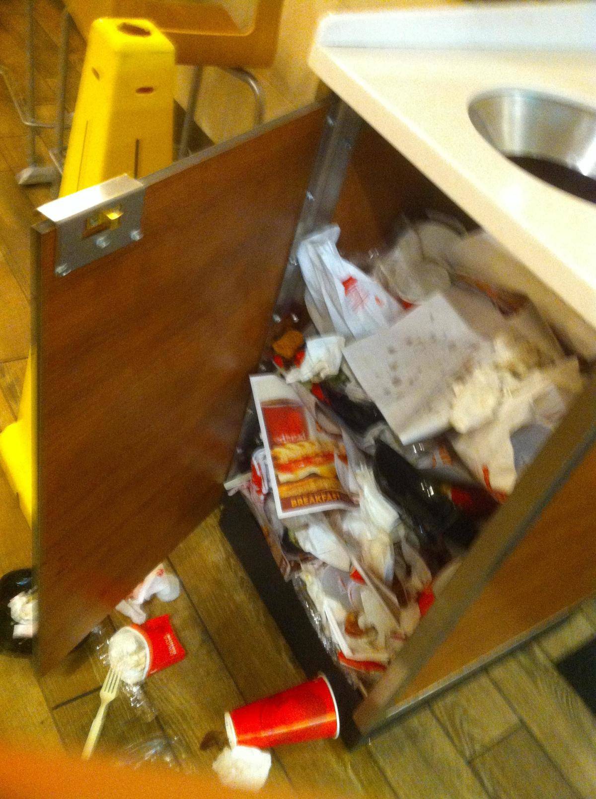 Trash overflowing out of wooden bin holder, no trash bin