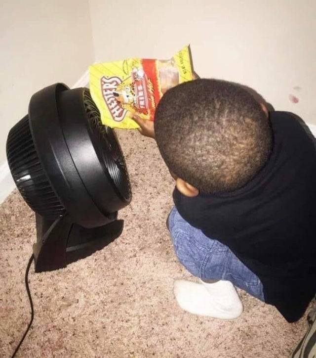 child crouched in front of fan holding bag of Cheetos to it