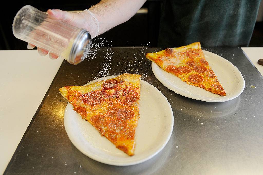 a person sprinkling parmesan on pizza