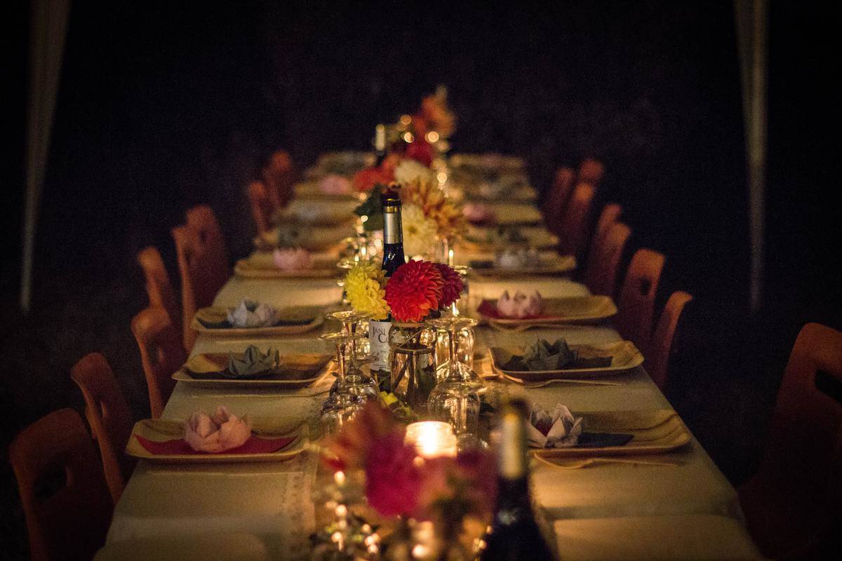 A long dinner table set with plates, napkins, wine, flowers, and candles.