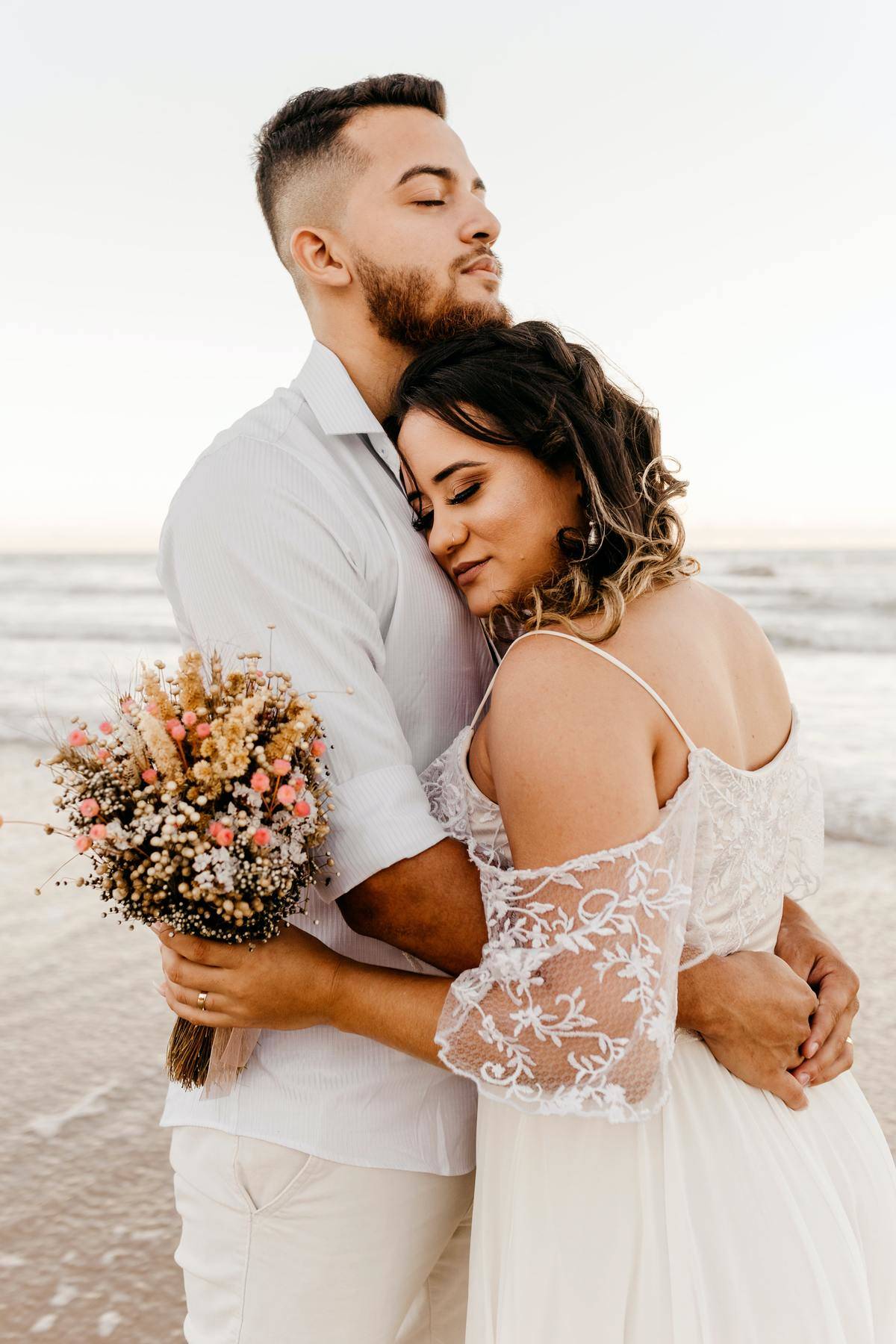 Newly married couple embrace each other while standing on the beach.