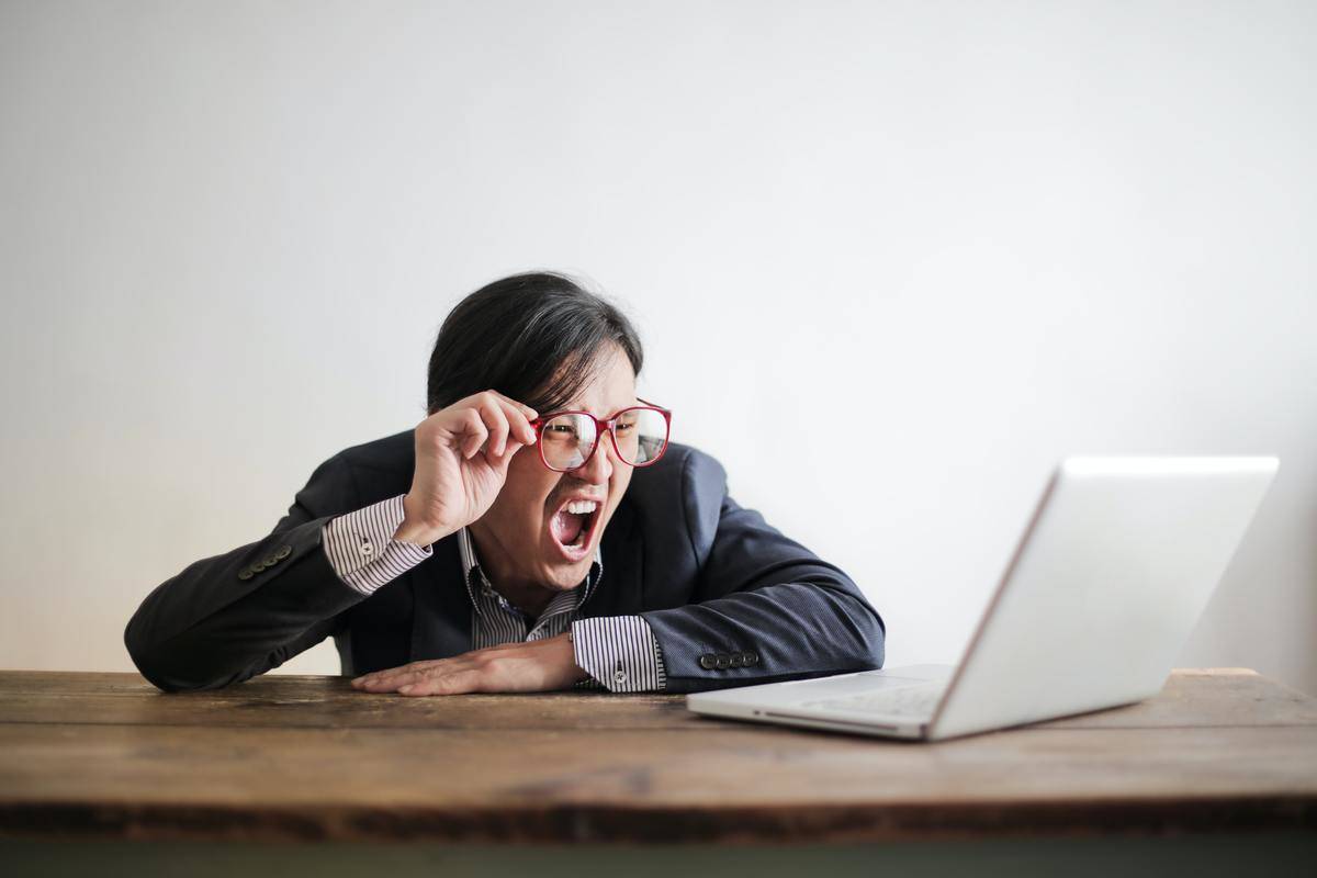 A man sits at a desk and yells at his laptop.