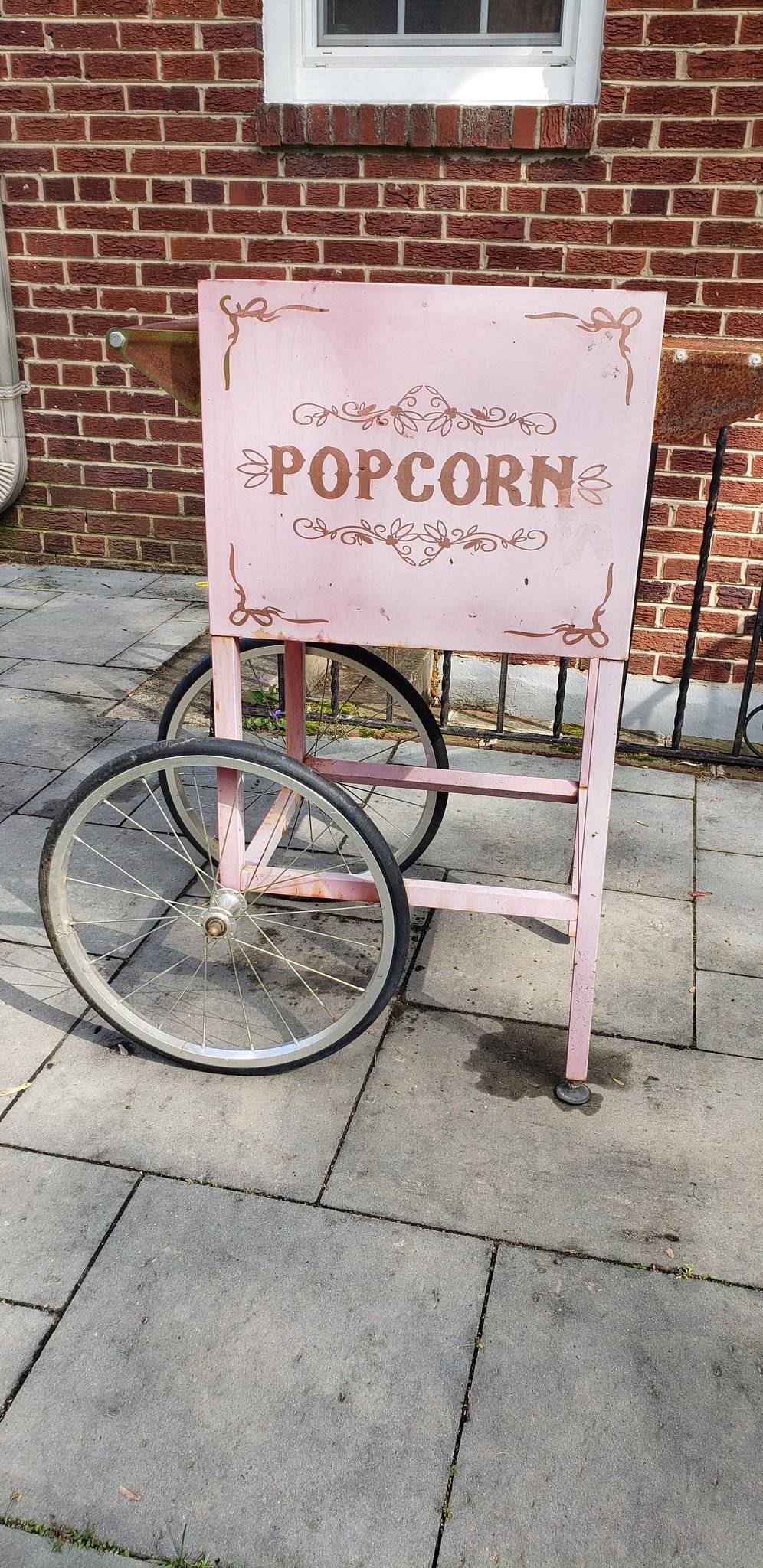 Pink popcorn cart on a sidewalk. 