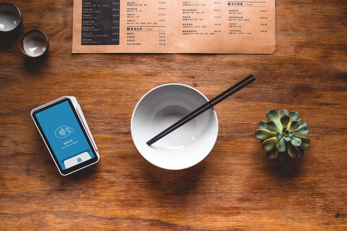 A dinner menu, empty bowl, chopsticks, and a card reader sit on top of a restaurant table.