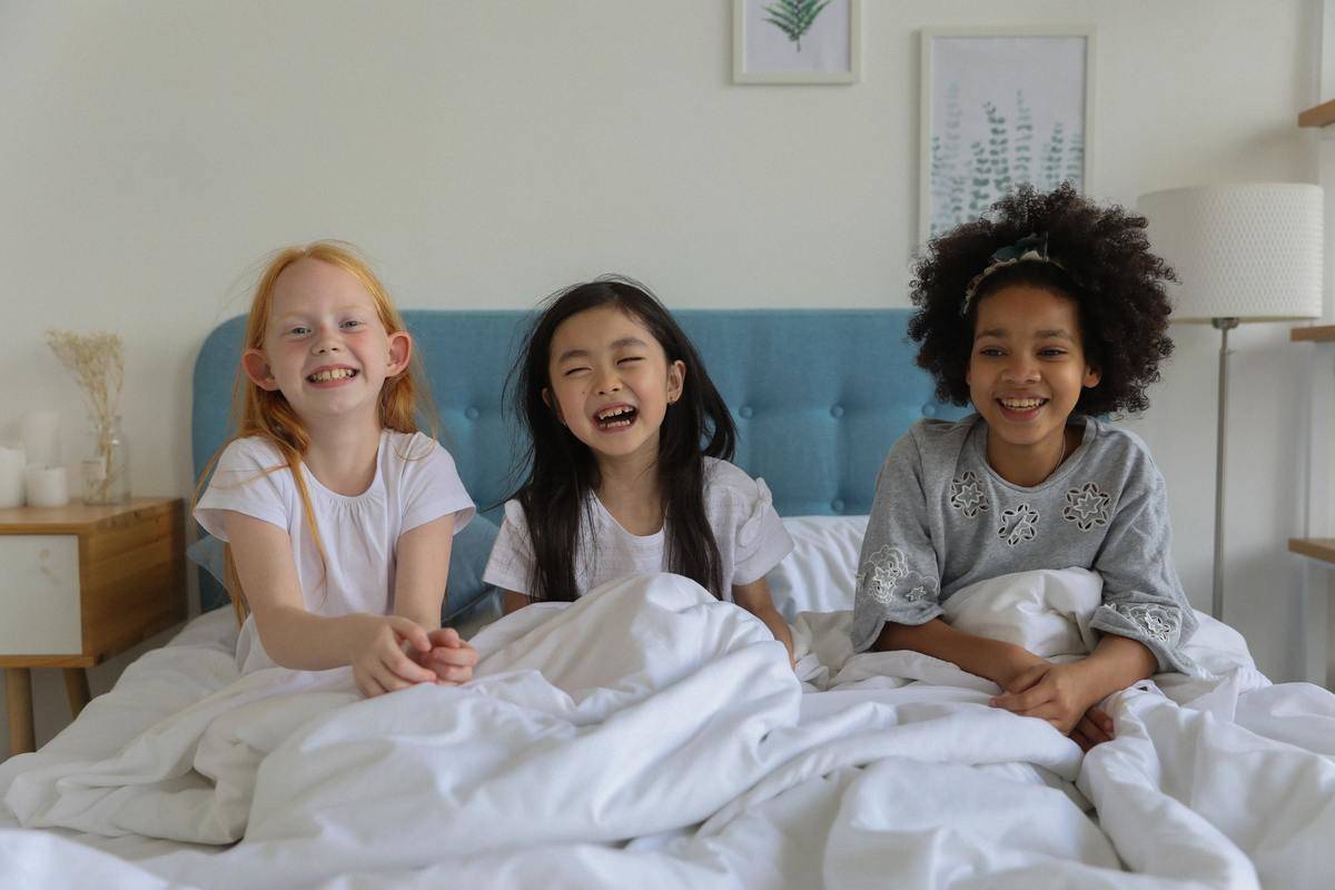 Three girls smile at the camera sitting in bed