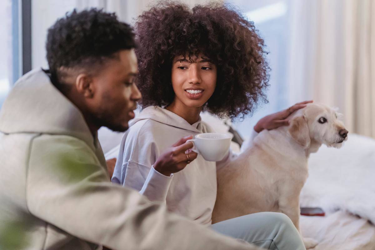 Woman looks at man as they sit on couch, she pets dog
