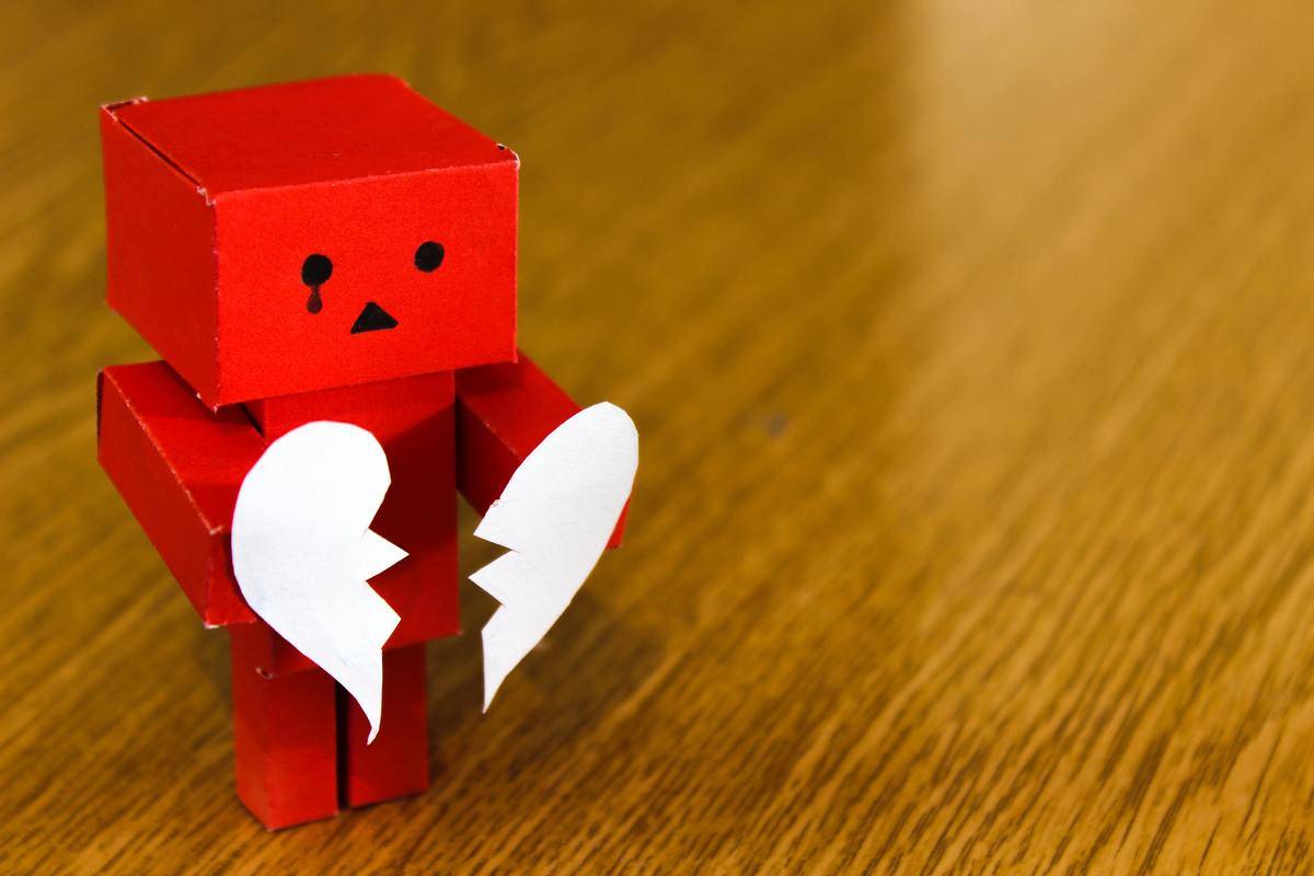 A tiny red robot made out of paper holds a heart that's broken in two.