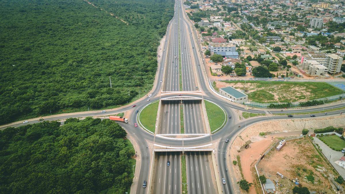 A major highway and city in Ghana on the right side of the photo, and lush green forests on the left side.