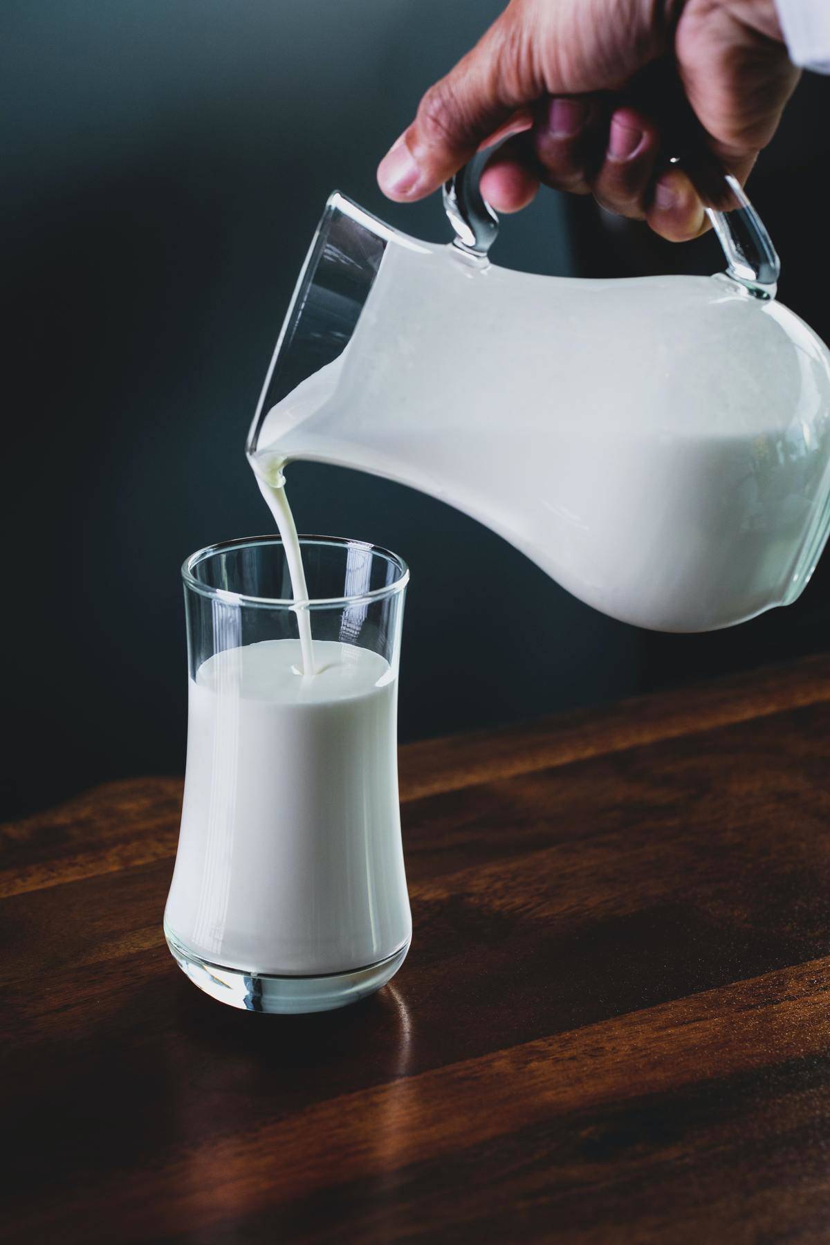 Person pours a cup of milk out of a glass jug.