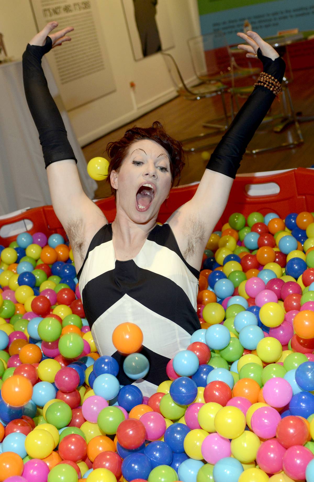 Woman in a ball pit with her hands above her head and hair under her armpits. 