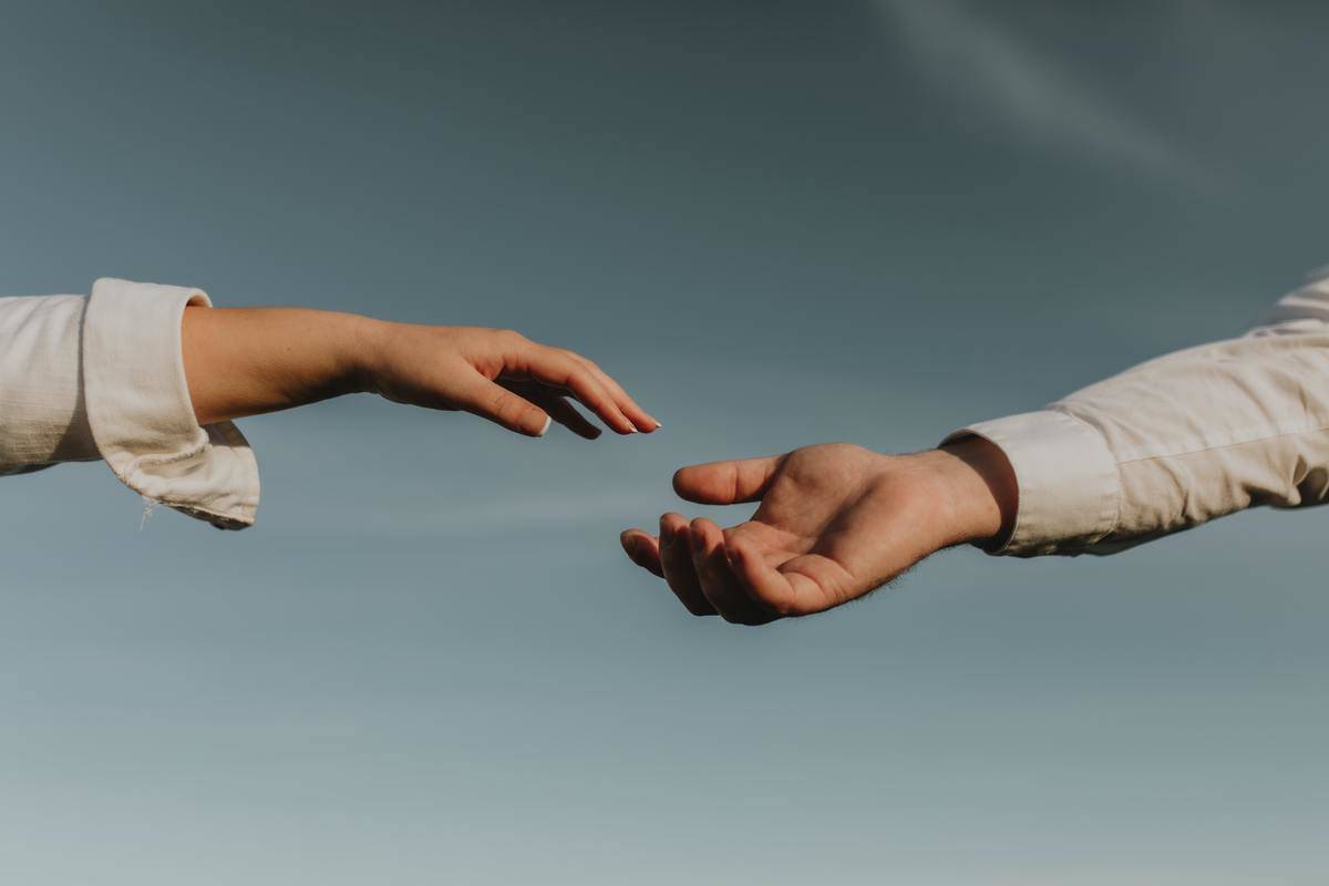two hands reaching for each other against a blue sky