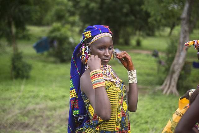 Woman with head dress on and lots of beaded bracelets.  