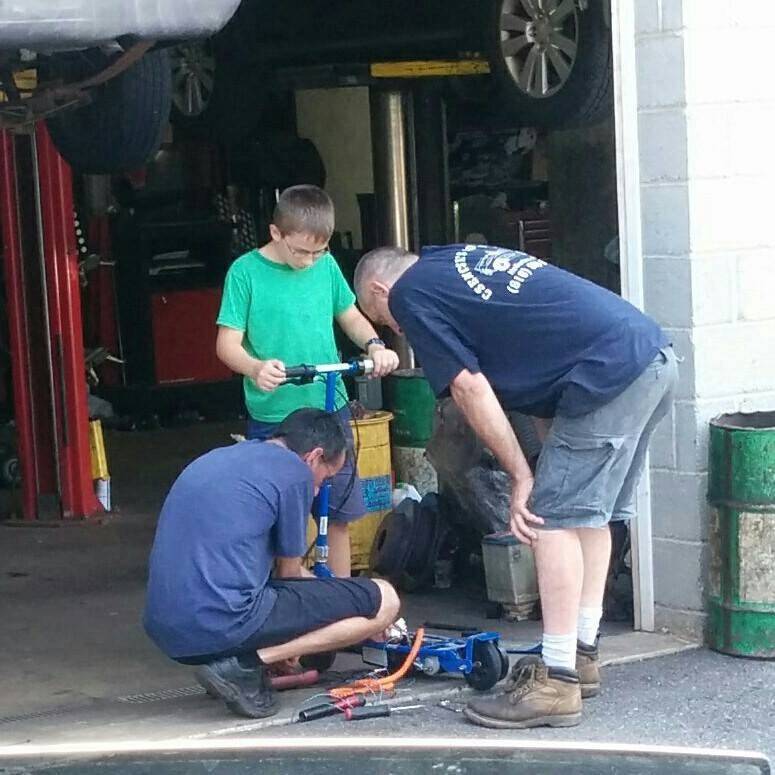 Scooter being worked on at local mechanic's shop, two mechanics and one young boy