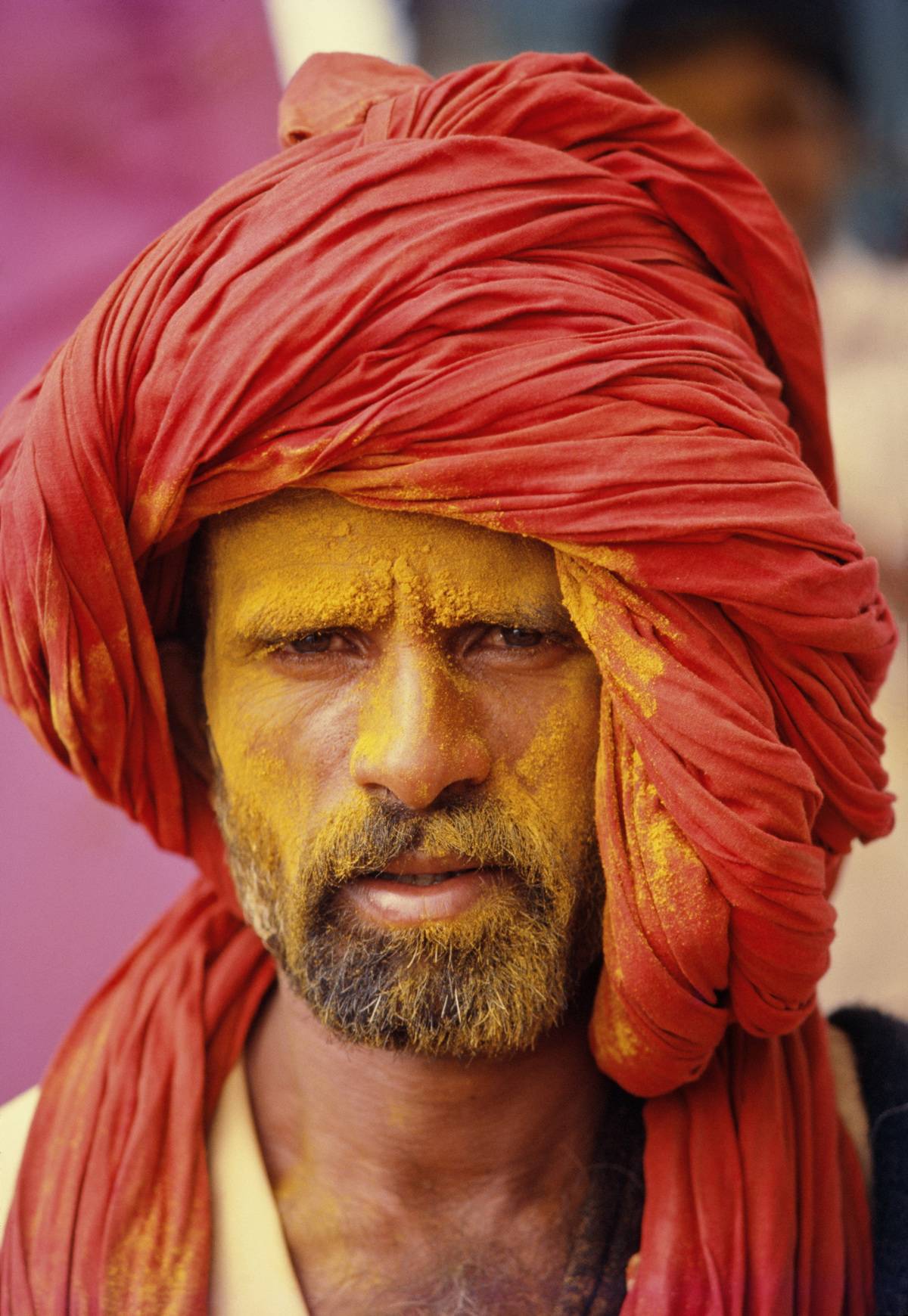 Man with yellow powder on face and red garb on his head. 