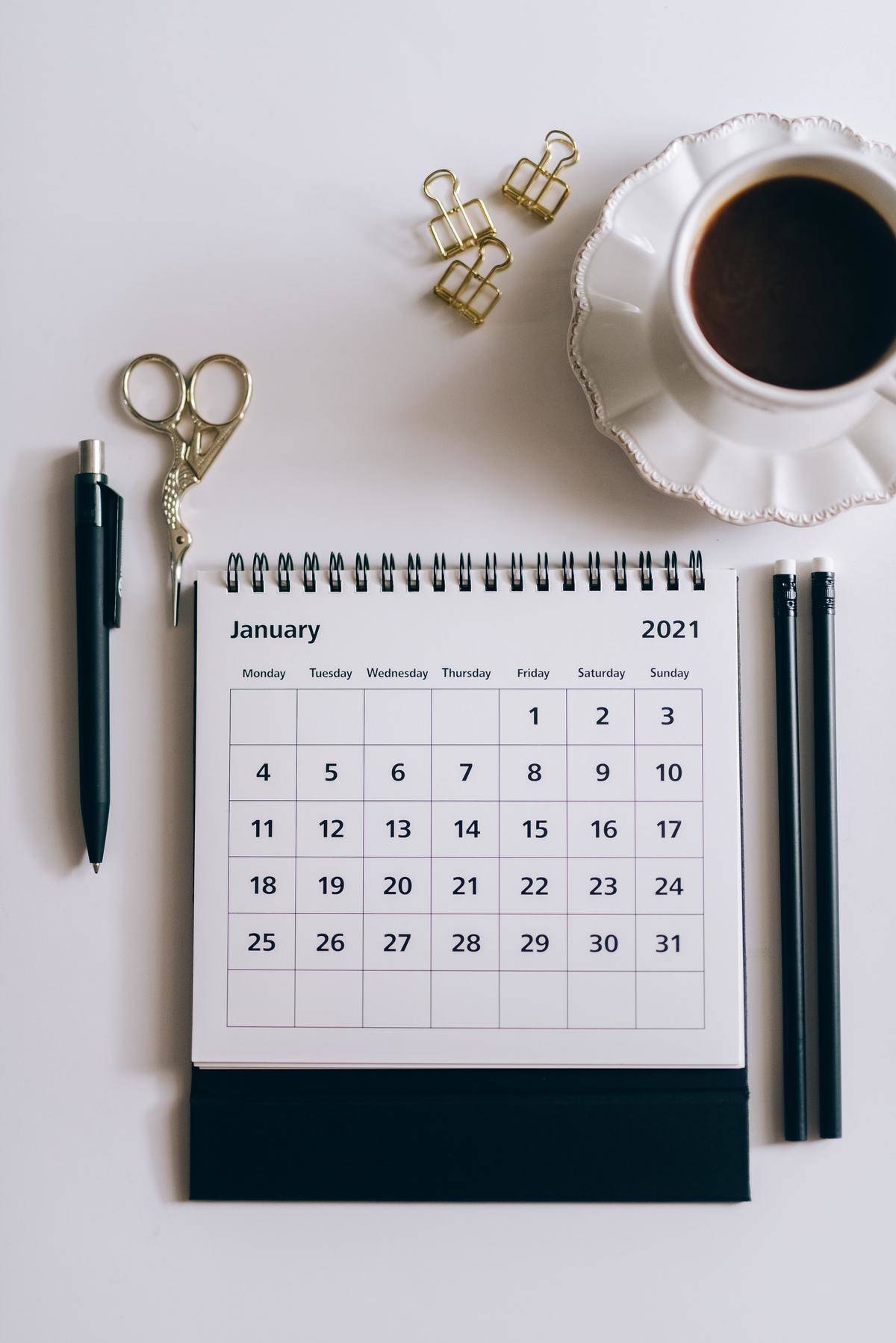 Close-up of a calendar on the month of January with a cup of tea and pens.