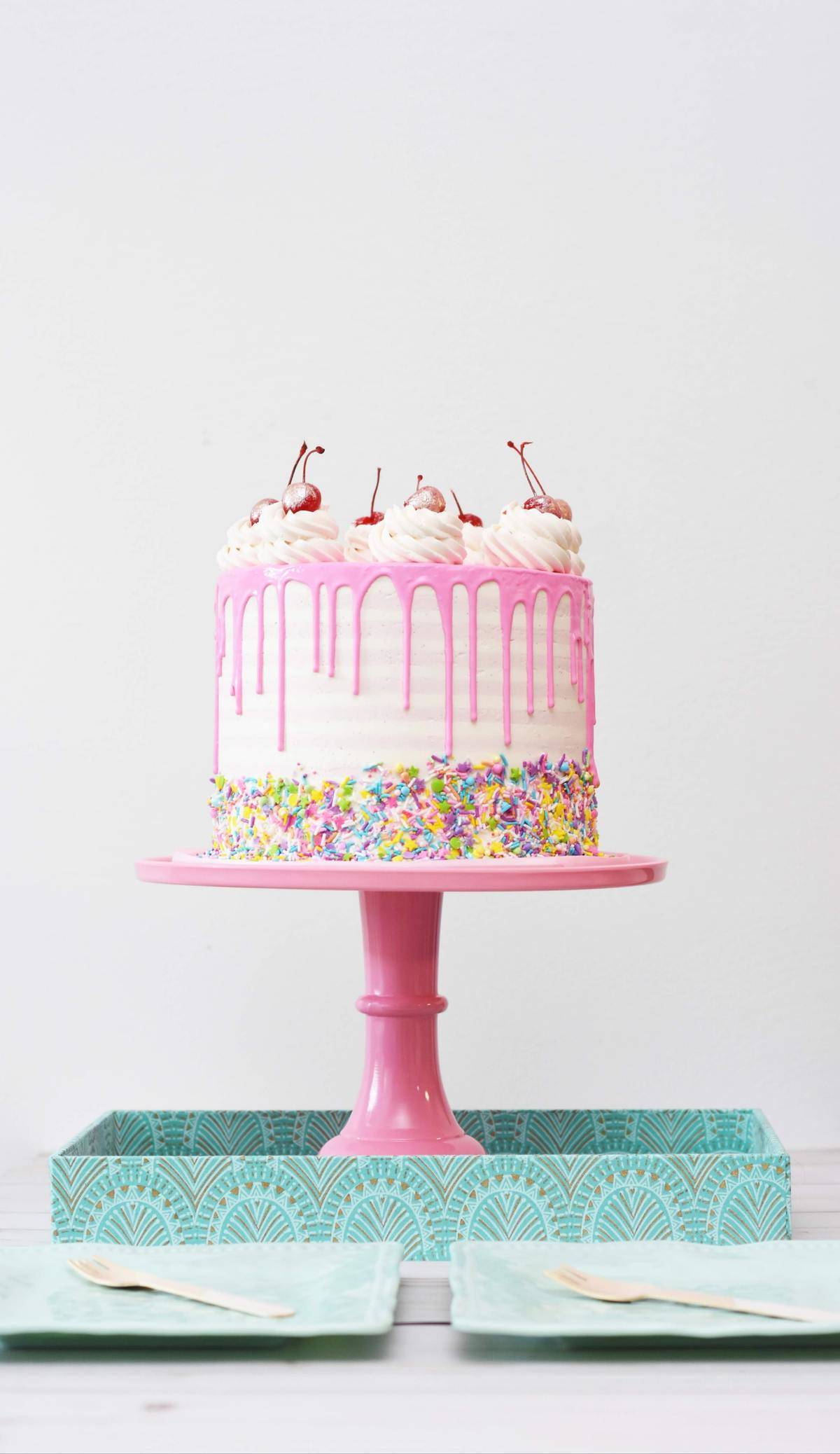 A pink birthday cake on a pink cake stand.