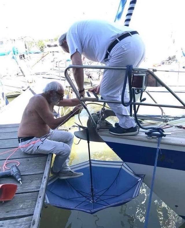 Two people working on a boat with an umbrella on the water to catch anything they drop