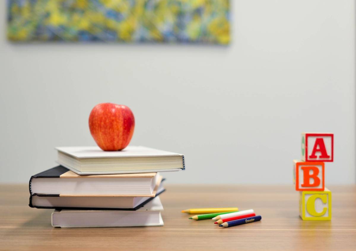 an apple on top of a stack of books with colored pencils and alphabet blocks