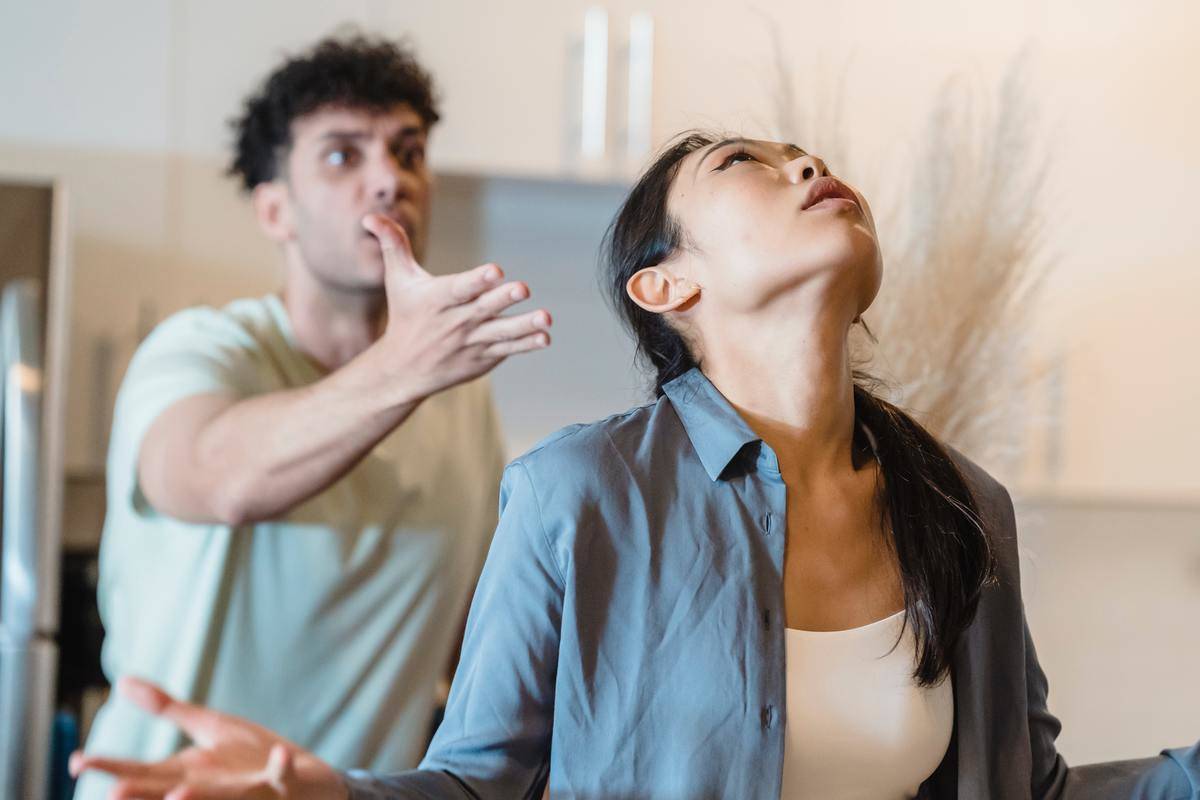 Woman annoyed, man behind her with his hand out palm raised upward