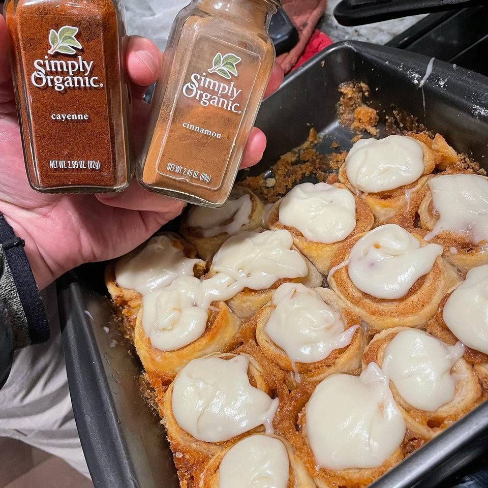 Tray of cinnamon buns and person holding up cayenne and cinnamon containers next to it