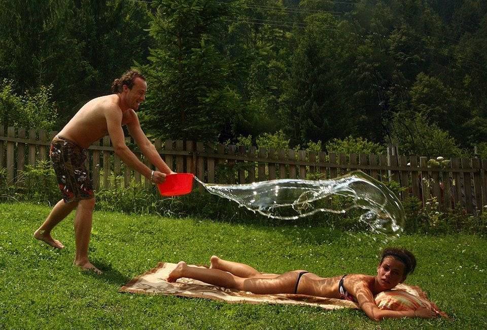 Woman tanning on lawn and man in bathing suit about to throw water on her.