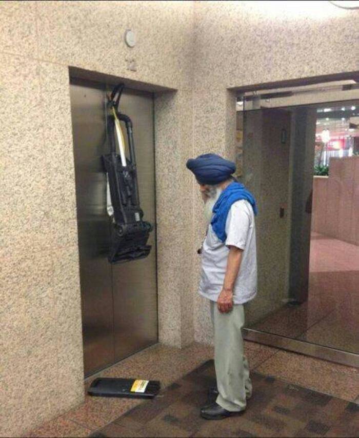 Corded vacuum gets stuck in an elevator and a man looks at it sadly.