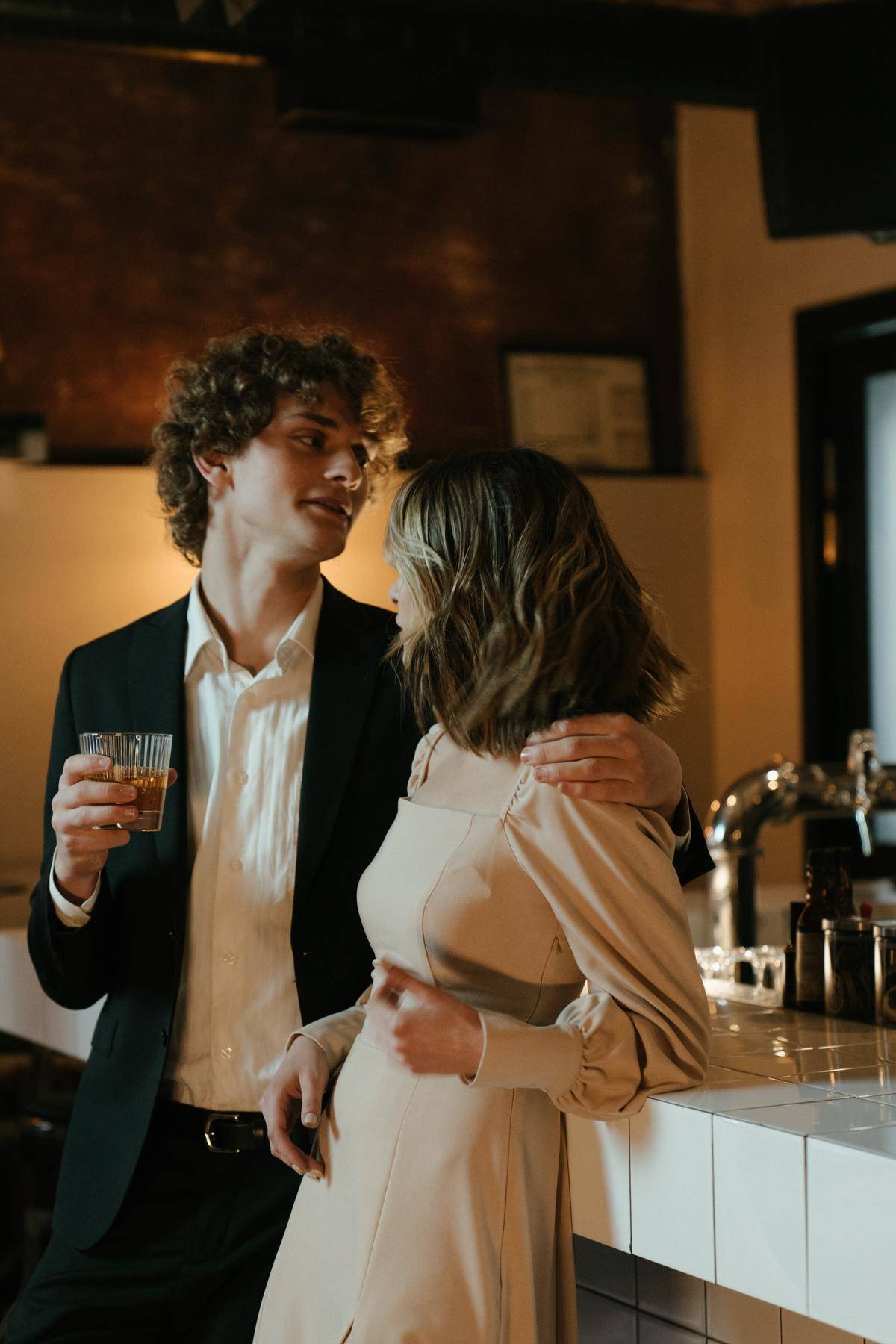 Man with his arm around woman's shoulders standing at restaurant bar