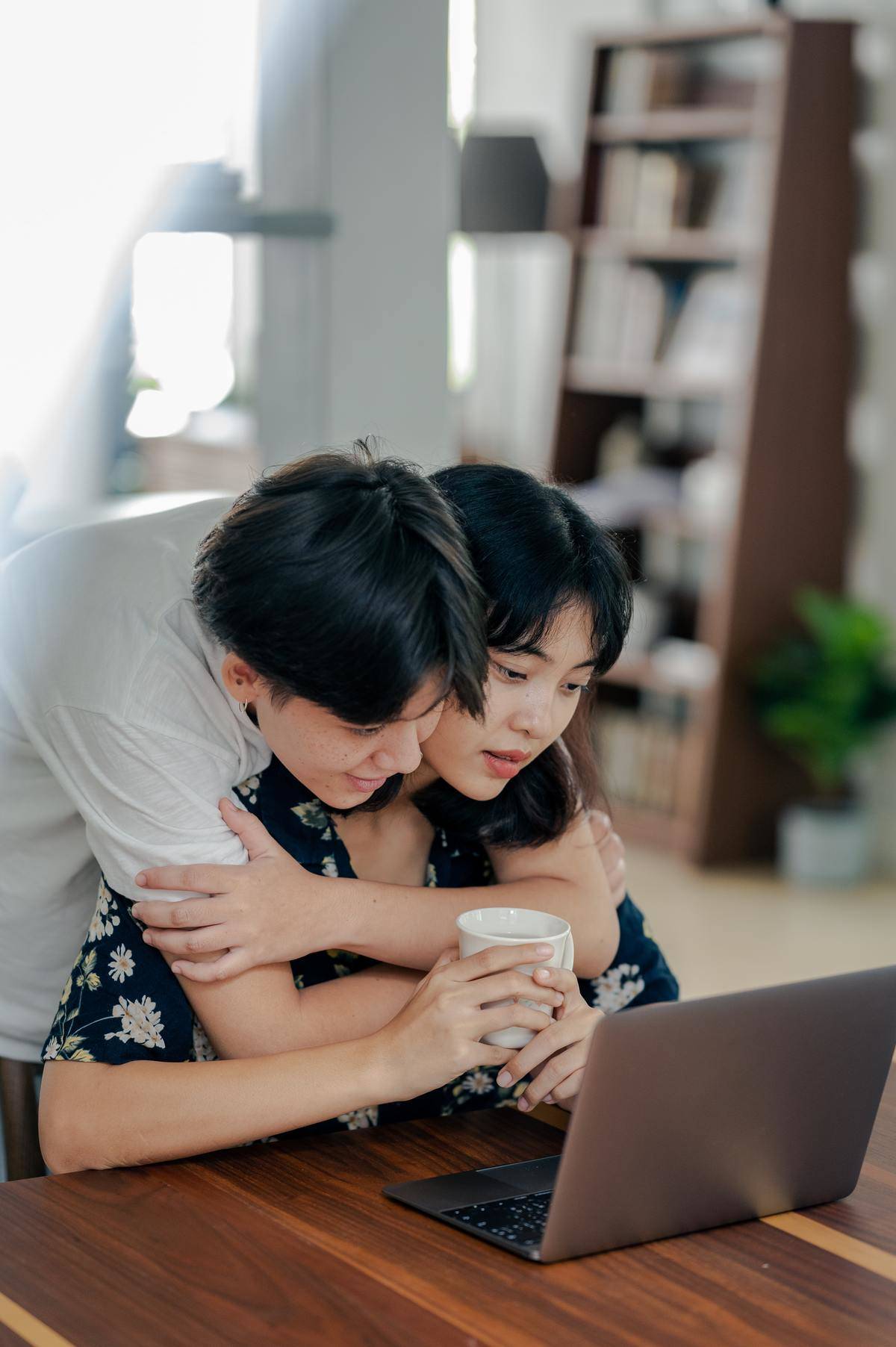 Couple sitting at table looking at laptop, man hugging woman from behind