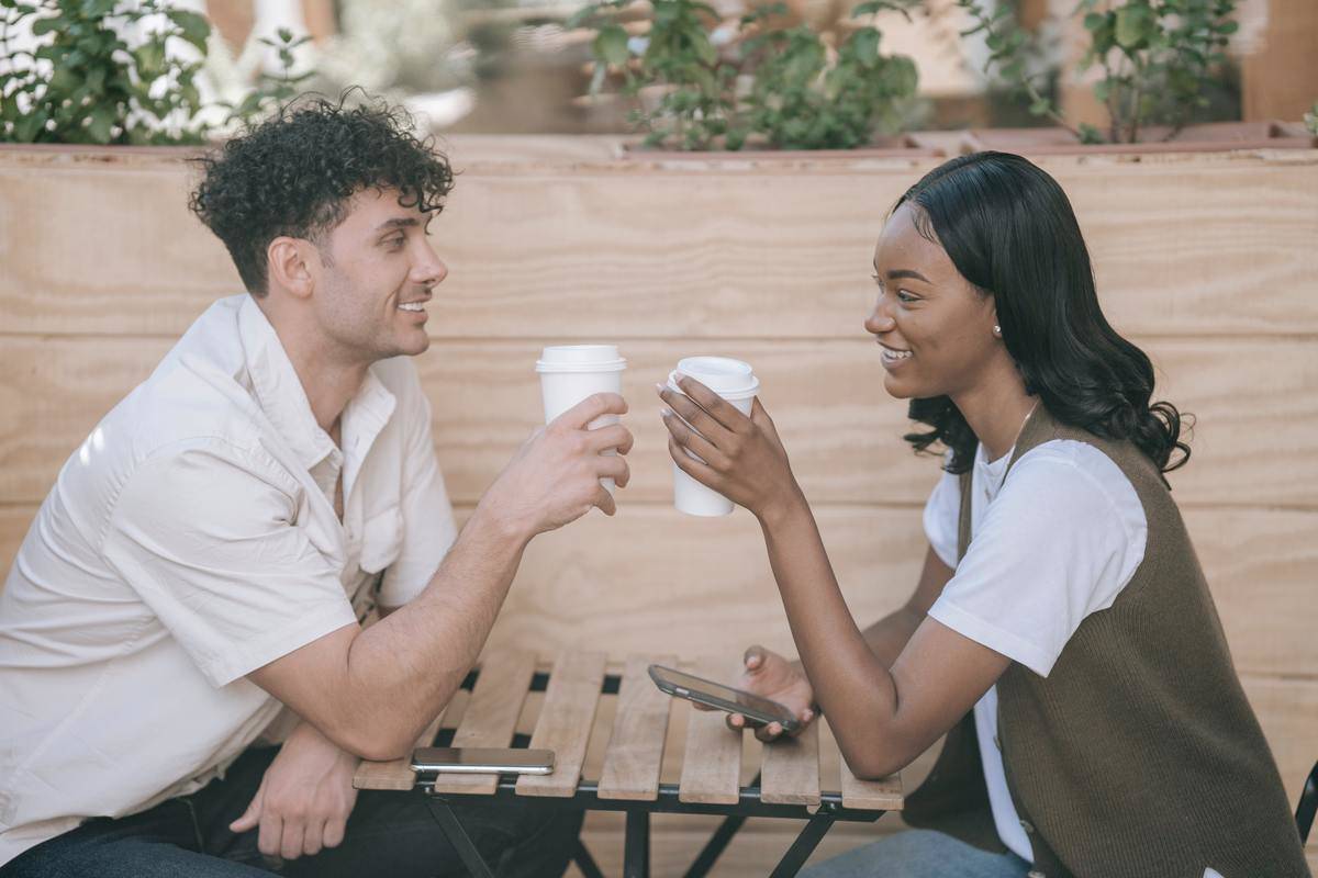 Couple smiles while sitting at table holding coffee cups