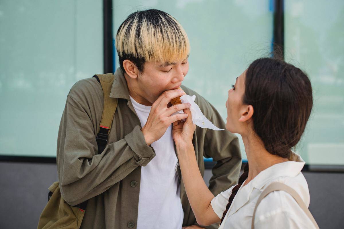 Woman holding hot dog for man who is taking a bite