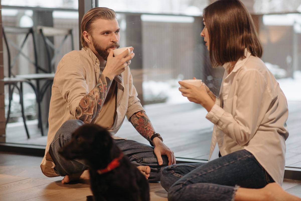 Man and woman sit on floor and talk; each with a cup of coffee