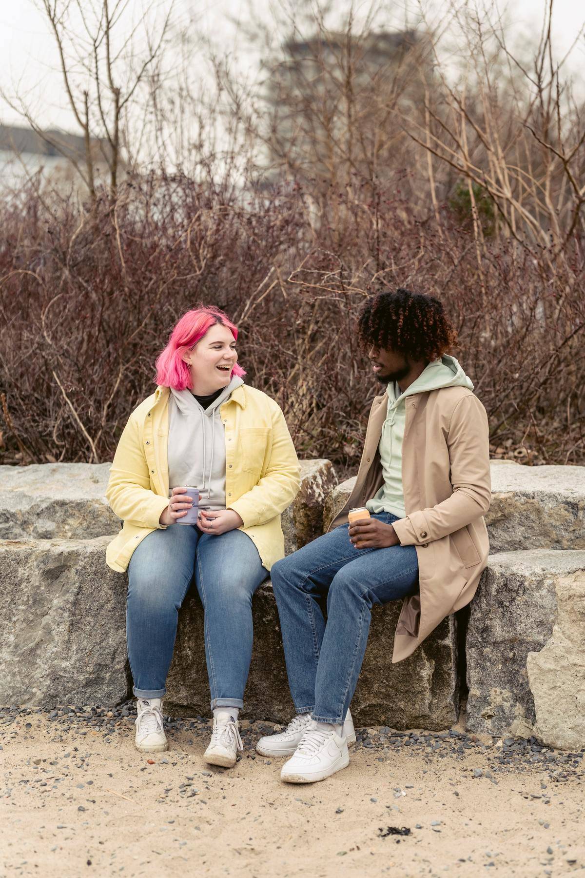 Couple sits on large stones outdoors and talks, woman has pink hair